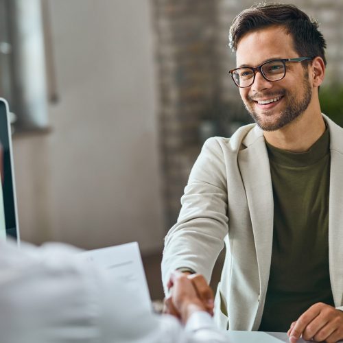 Happy male candidate handshaking with a manager after successful job interview in the office.